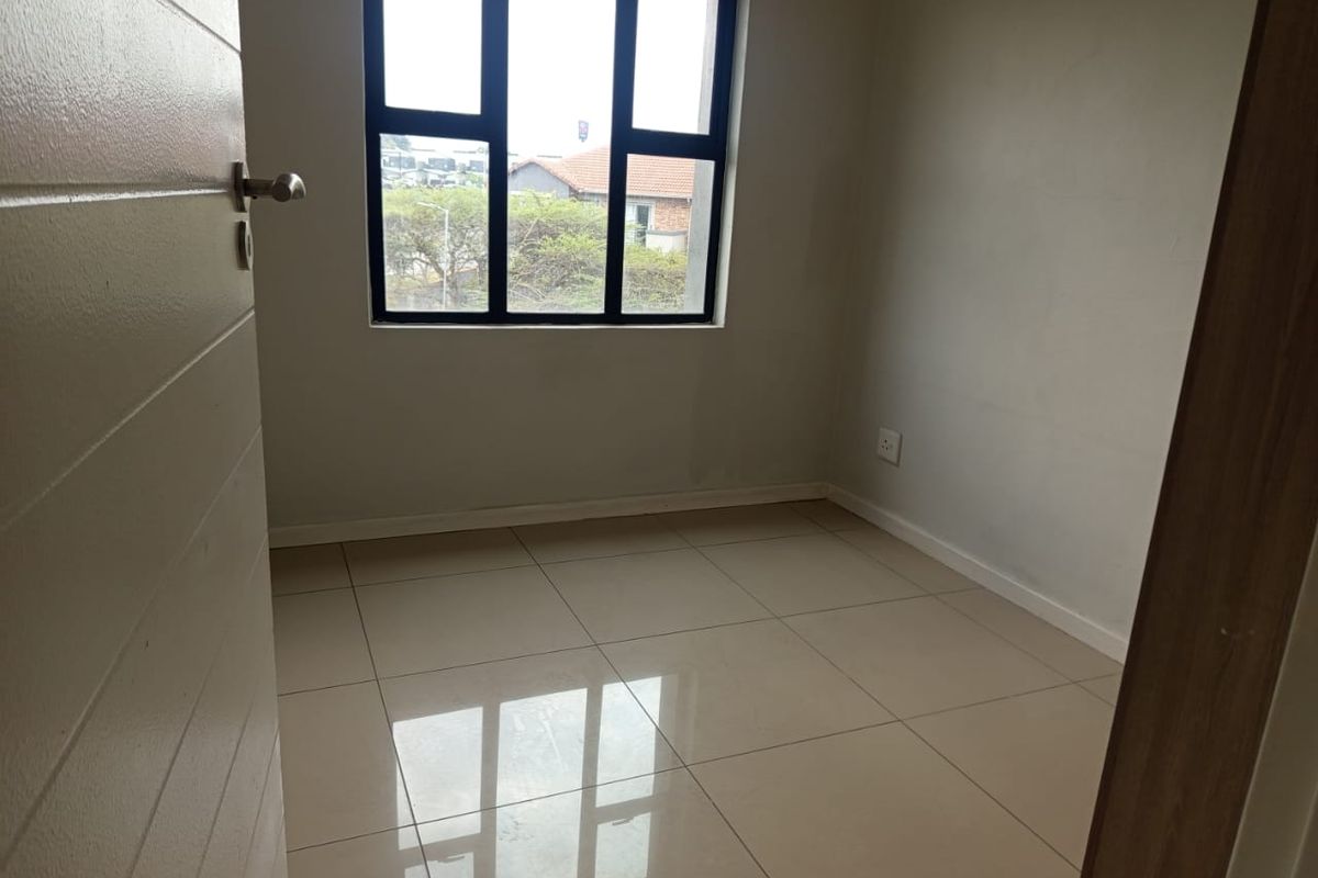 A bright, empty bedroom featuring neutral tiled flooring and a large black-framed window, offering a clean and versatile space ready for furnishing.
