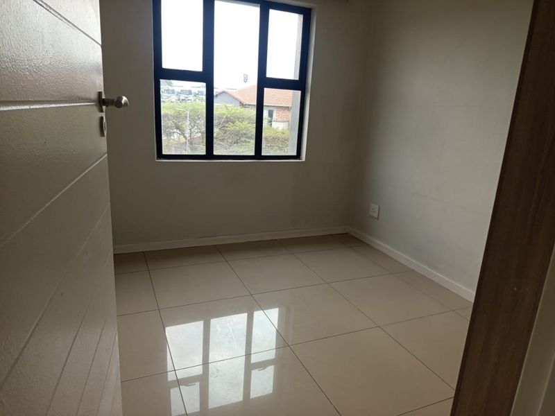 A bright, empty bedroom featuring neutral tiled flooring and a large black-framed window, offering a clean and versatile space ready for furnishing.