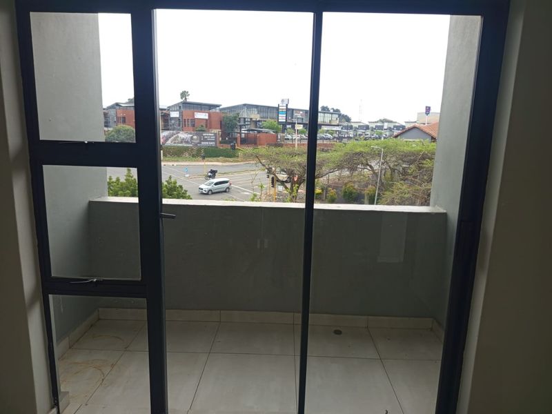A compact balcony featuring tiled flooring and a concrete balustrade, offering an elevated view of the surrounding neighborhood and street.