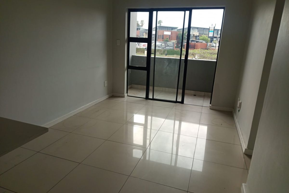 An empty, well-lit living area featuring neutral porcelain floor tiles and a large sliding glass door providing direct access to a private balcony.