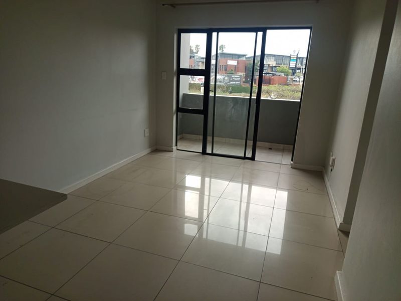 An empty, well-lit living area featuring neutral porcelain floor tiles and a large sliding glass door providing direct access to a private balcony.