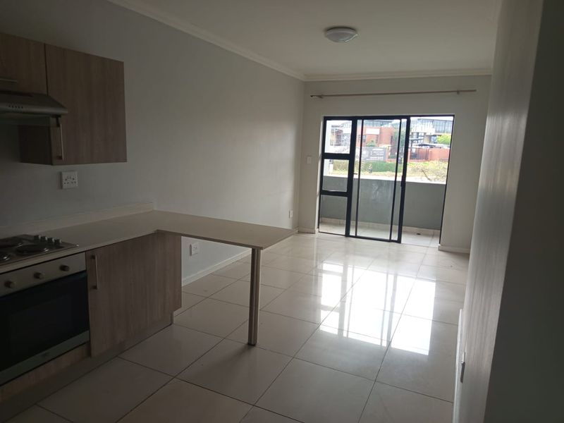 Open-plan kitchen and living area featuring tiled floors, built-in cabinetry with integrated appliances, and access to a private balcony through sliding glass doors.