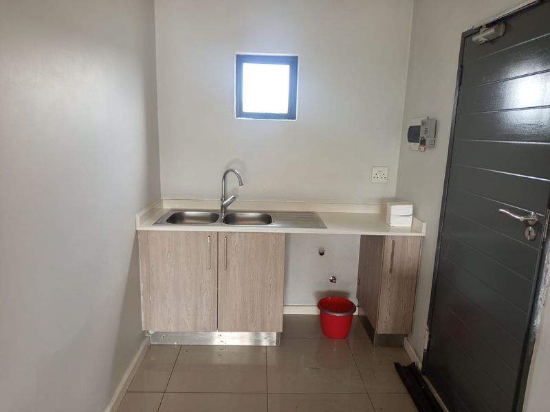 A functional scullery area featuring a double bowl stainless steel sink, laminate cabinetry, and tiled flooring, with visible plumbing connections for appliances.