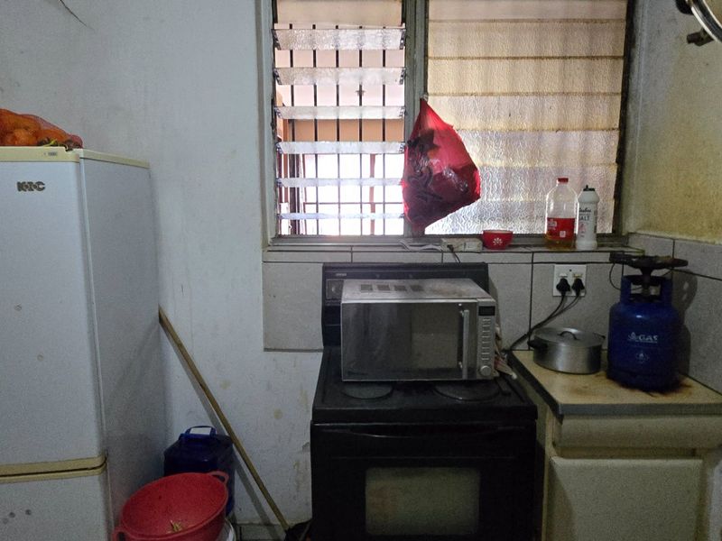A compact kitchen area featuring a built-in stove and oven, tiled splashback, and louver window, currently requiring significant maintenance and cosmetic updates.