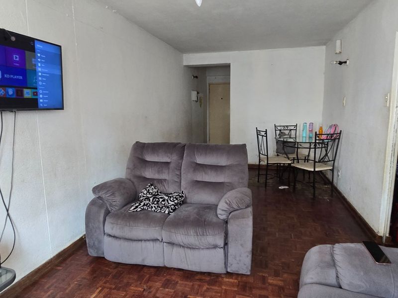 Open-plan living and dining area featuring parquet flooring and wall-mounted television setup, requiring cosmetic updates to wall finishes and flooring.