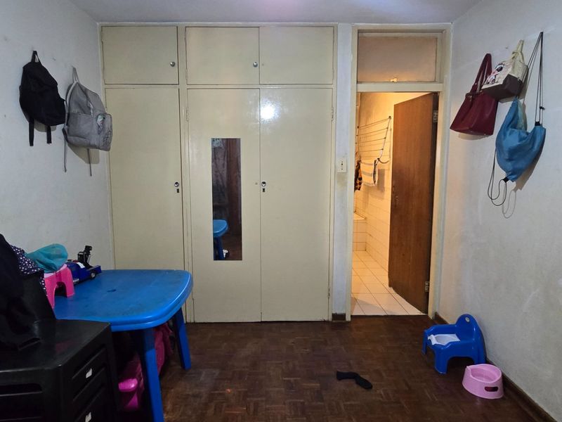 Bedroom featuring built-in cupboards and parquet flooring, requiring cosmetic updates to the wall finishes and general maintenance.
