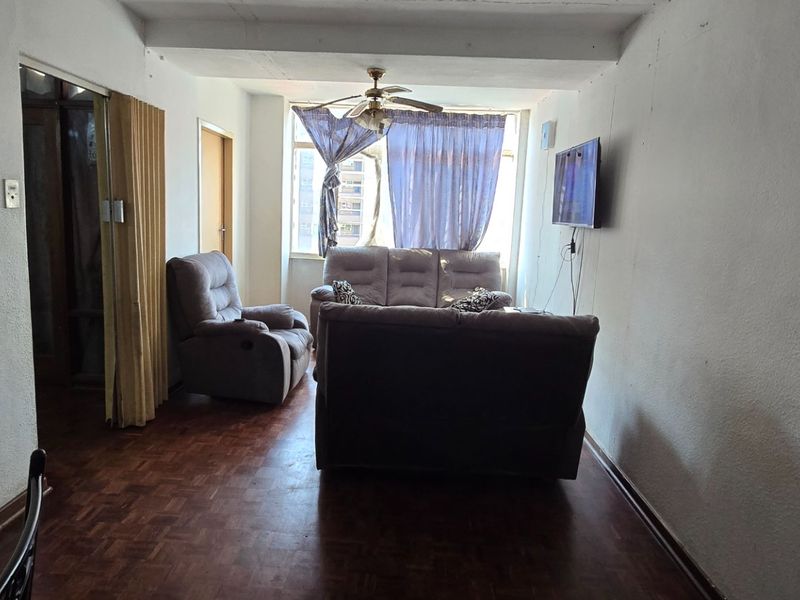 A living room featuring parquet flooring, a ceiling fan, and a folding door, providing a functional space with potential for cosmetic updates.