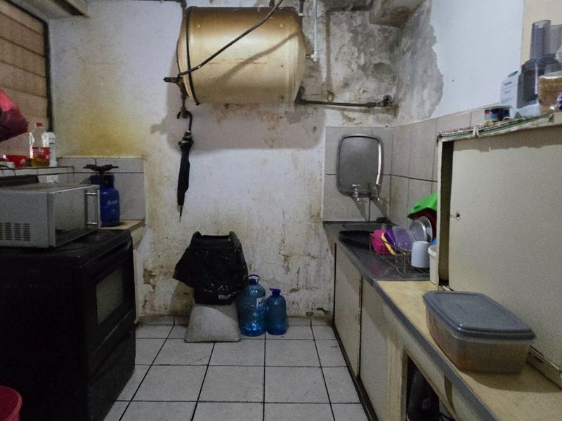 A dated kitchen area featuring built-in cabinetry, a stainless steel sink, and an exposed electric water heater, requiring significant renovation and cosmetic repairs.