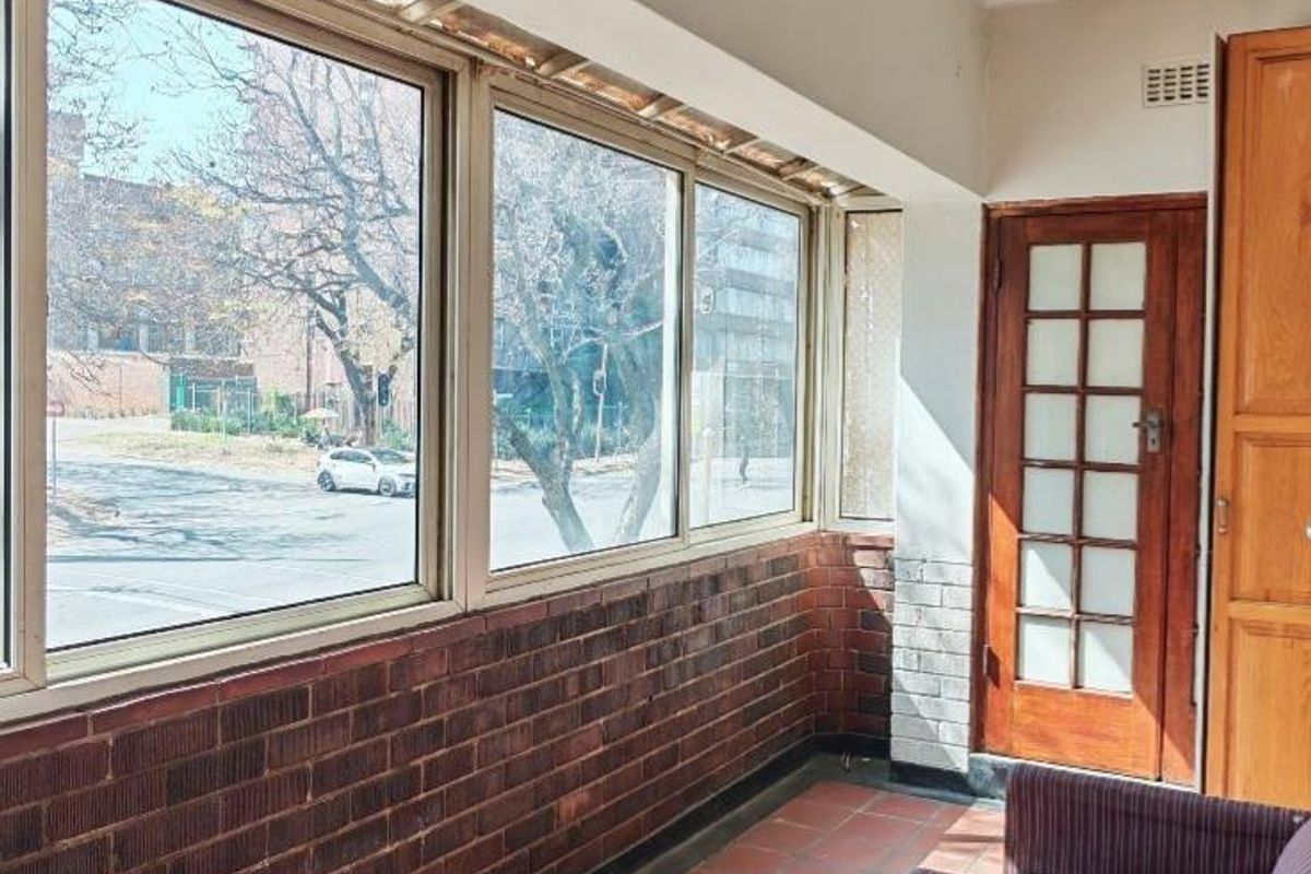 Enclosed balcony featuring terracotta tile flooring, exposed brickwork, and large windows providing natural light and street views.