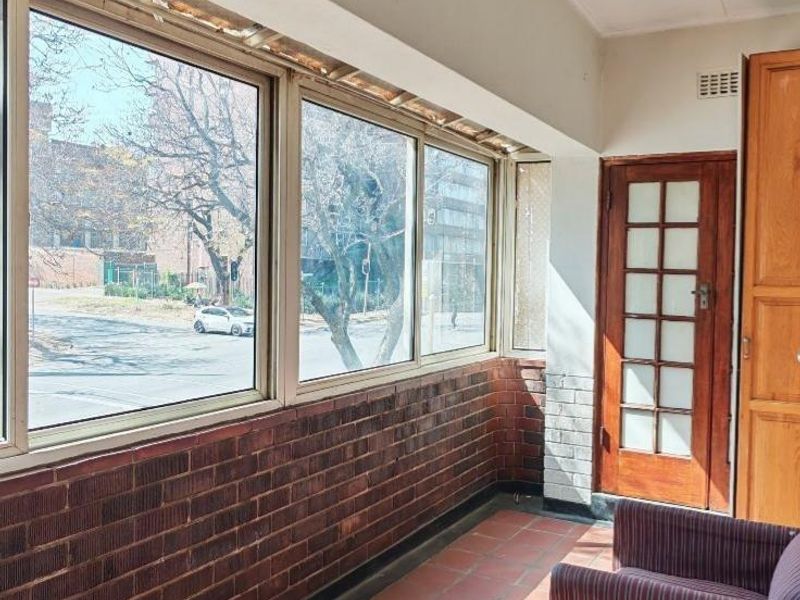 Enclosed balcony featuring terracotta tile flooring, exposed brickwork, and large windows providing natural light and street views.