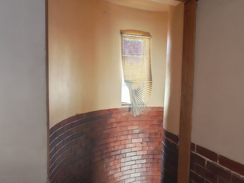 A spiral staircase area featuring exposed brick walls, timber door framing, and tiled flooring, currently showing signs of wear and requiring maintenance.