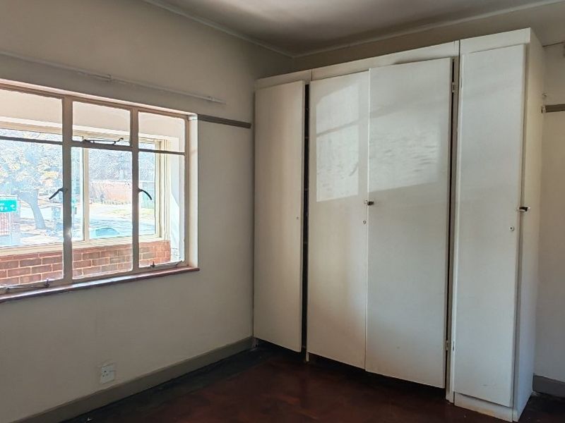 An empty bedroom featuring original parquet flooring, a built-in wardrobe, and a steel-framed window with natural light.