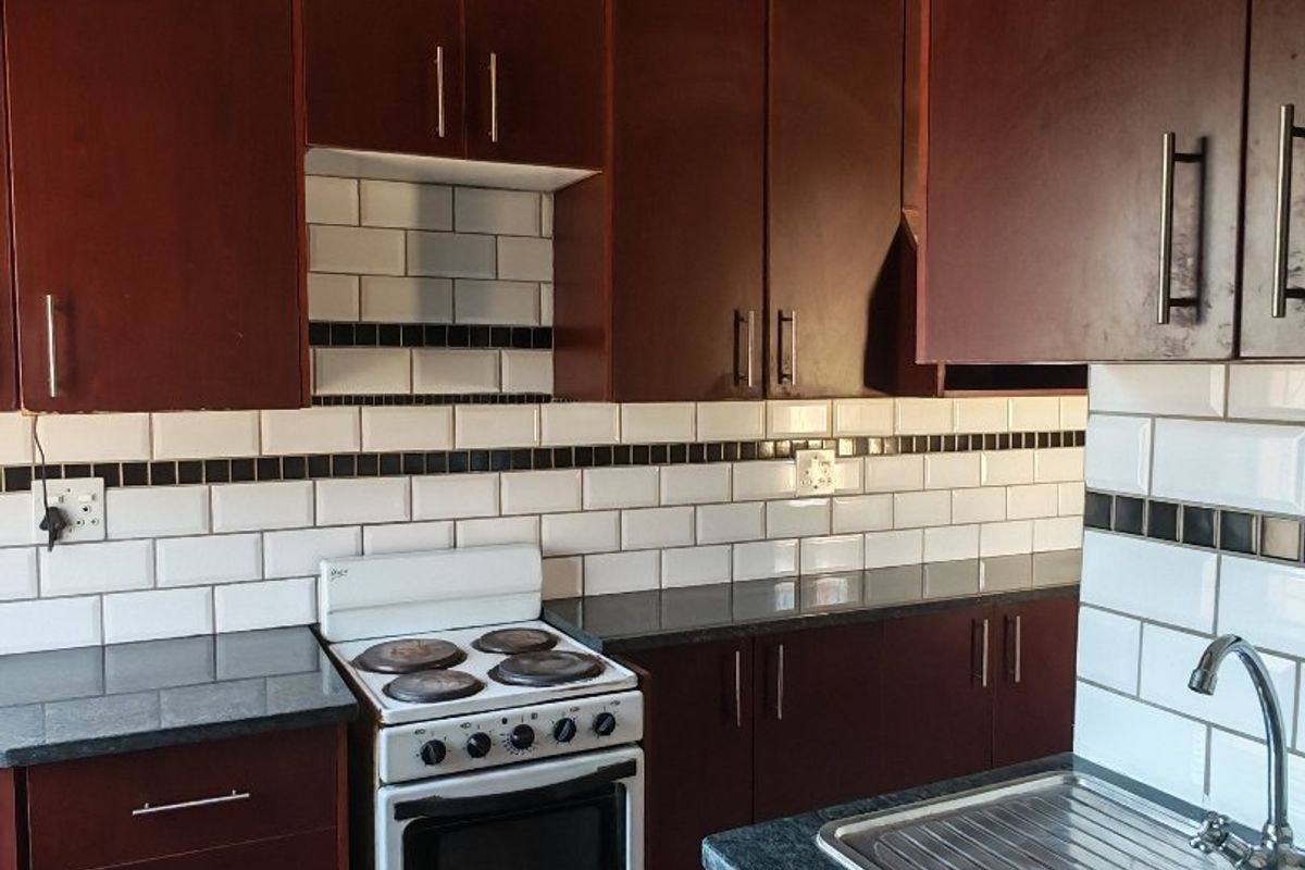 A functional kitchen featuring dark wood cabinetry, granite countertops, a subway tile backsplash, and a freestanding electric stove with terracotta flooring.