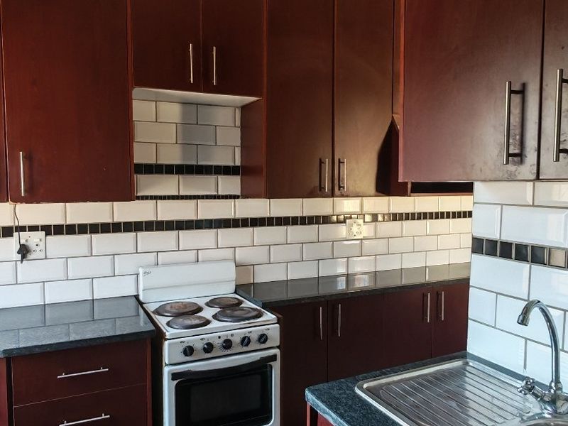 A functional kitchen featuring dark wood cabinetry, granite countertops, a subway tile backsplash, and a freestanding electric stove with terracotta flooring.