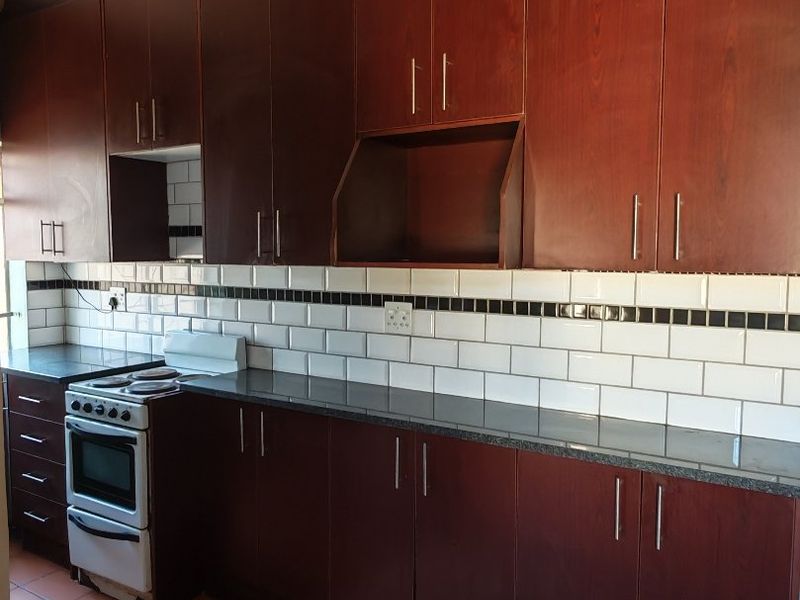 A functional kitchen featuring dark wood cabinetry, granite countertops, a classic subway tile backsplash, and tiled flooring.