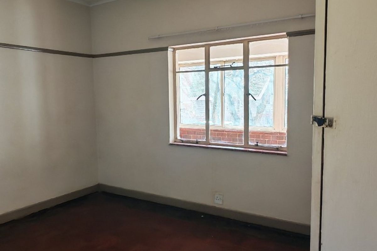 An empty bedroom featuring original parquet flooring, a picture rail, and a built-in cupboard, offering a blank canvas for renovation.