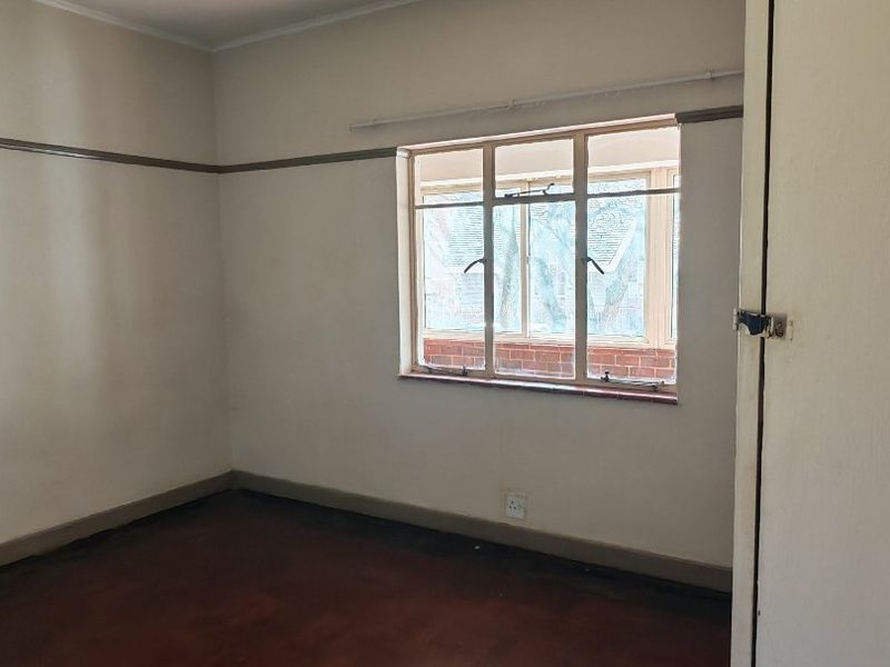An empty bedroom featuring original parquet flooring, a picture rail, and a built-in cupboard, offering a blank canvas for renovation.