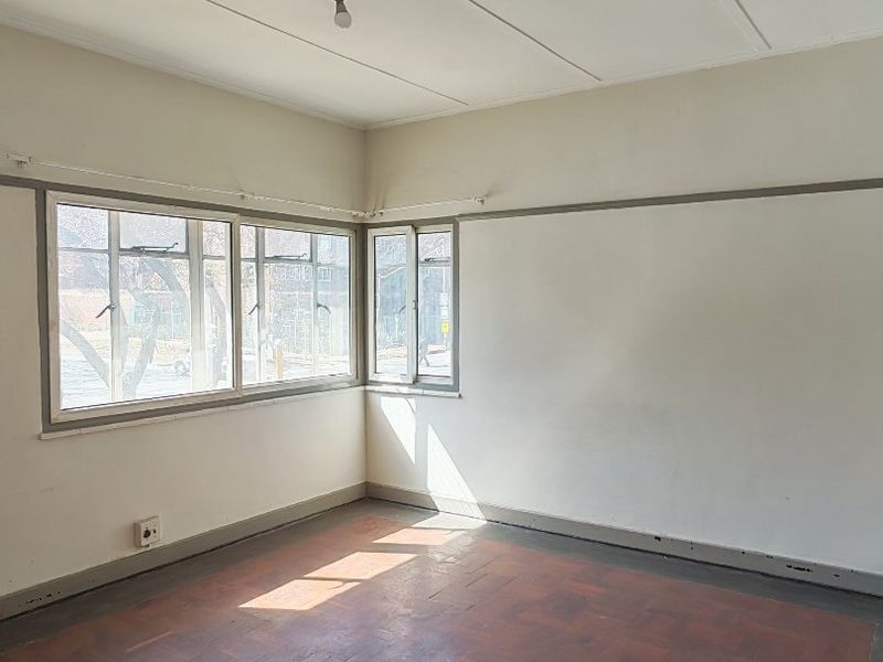 An empty bedroom featuring original parquet flooring, steel-framed windows, and a classic picture rail, offering a blank canvas for renovation.