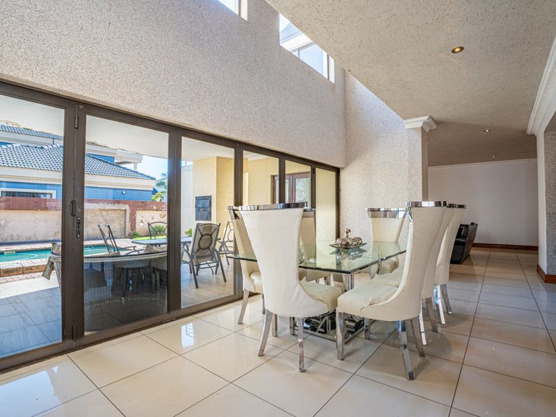 Spacious open-plan dining area featuring double-volume ceilings, large format floor tiles, and expansive aluminium sliding doors providing seamless access to the outdoor pool area.
