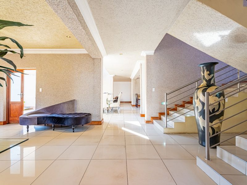 Spacious entrance hall featuring tiled flooring, a modern staircase with stainless steel balustrades, and textured wall finishes leading into the open-plan living area.