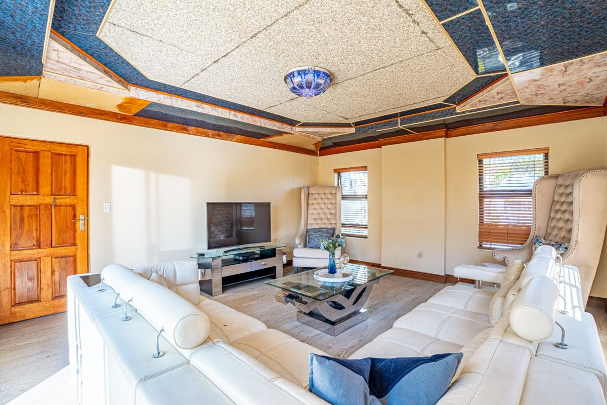 A living room featuring laminate flooring, a distinctive coffered ceiling design, and natural light through windows with fitted venetian blinds.
