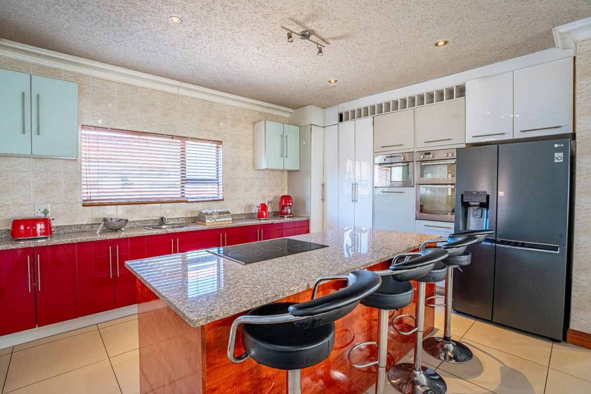 Modern kitchen featuring vibrant red cabinetry, granite countertops, a central island with an integrated hob, and built-in appliances including an oven and microwave.