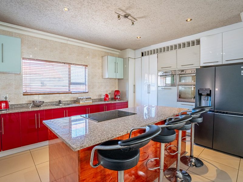 Modern kitchen featuring vibrant red cabinetry, granite countertops, a central island with an integrated hob, and built-in appliances including an oven and microwave.