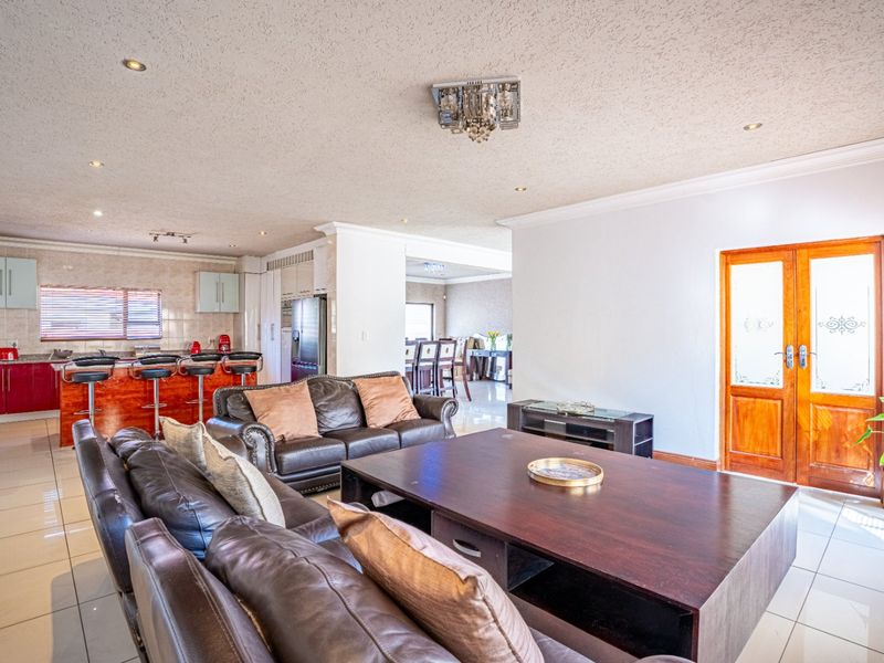 Spacious open-plan living area featuring tiled floors, recessed lighting, and a modern kitchen with a breakfast island, seamlessly connecting to adjacent dining spaces.