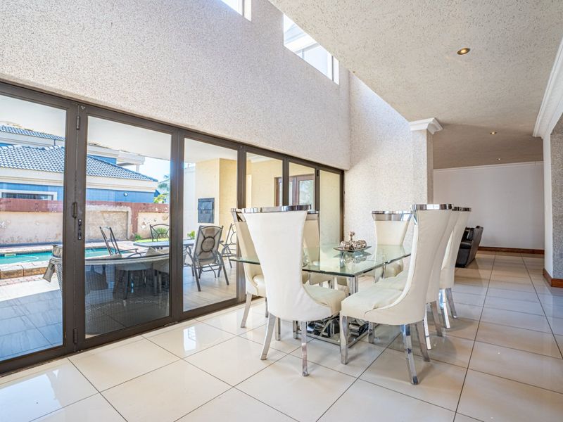 Spacious dining area featuring double volume ceilings, large format floor tiles, and expansive aluminium sliding doors providing seamless access to the outdoor pool area.