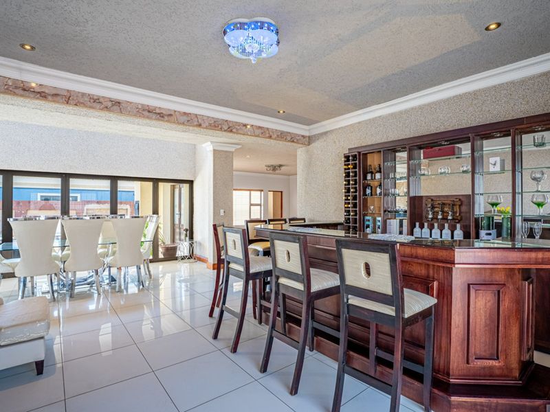 Spacious entertainment area featuring a custom built-in wooden bar with integrated shelving and glass display cabinets, complemented by polished tiled flooring.