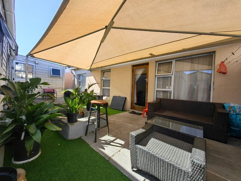 Outdoor patio area featuring a large shade sail, paved flooring, and artificial grass sections, providing a functional space for outdoor relaxation.