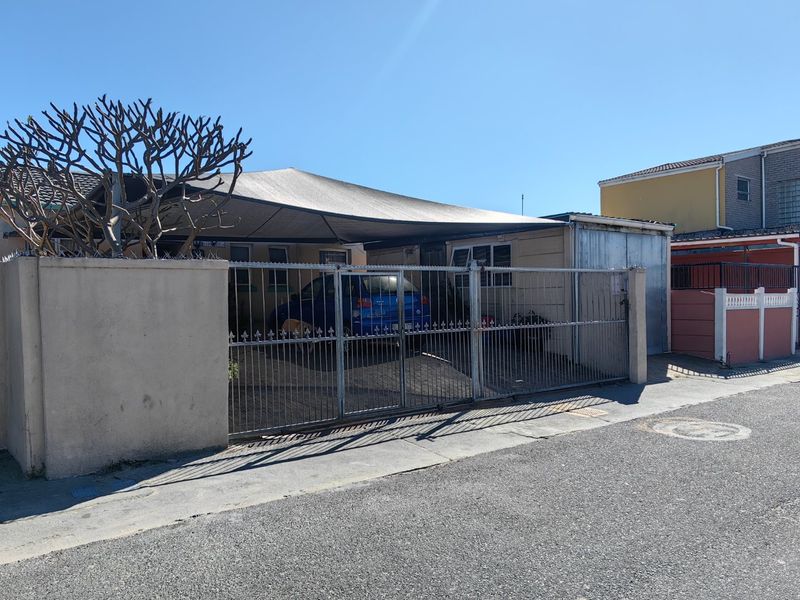 Front exterior view of the property featuring a paved driveway, metal security gate, perimeter wall with razor wire, and a shade cloth carport structure.