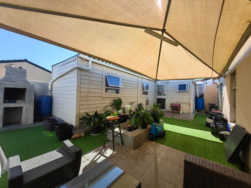 Outdoor patio area featuring a shade sail, built-in braai, and artificial lawn, providing a functional space for outdoor entertaining.