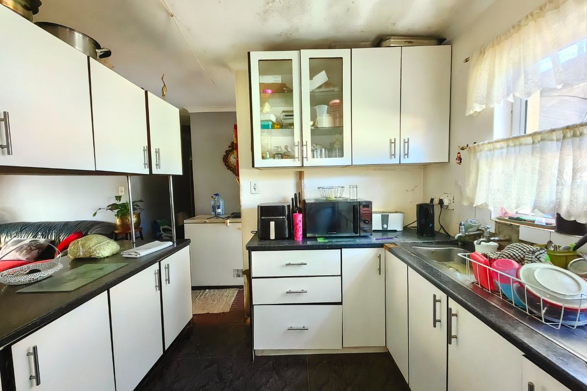 A functional kitchen featuring white cabinetry, dark countertops, and tiled flooring, currently showing signs of ceiling wear and requiring cosmetic updates.