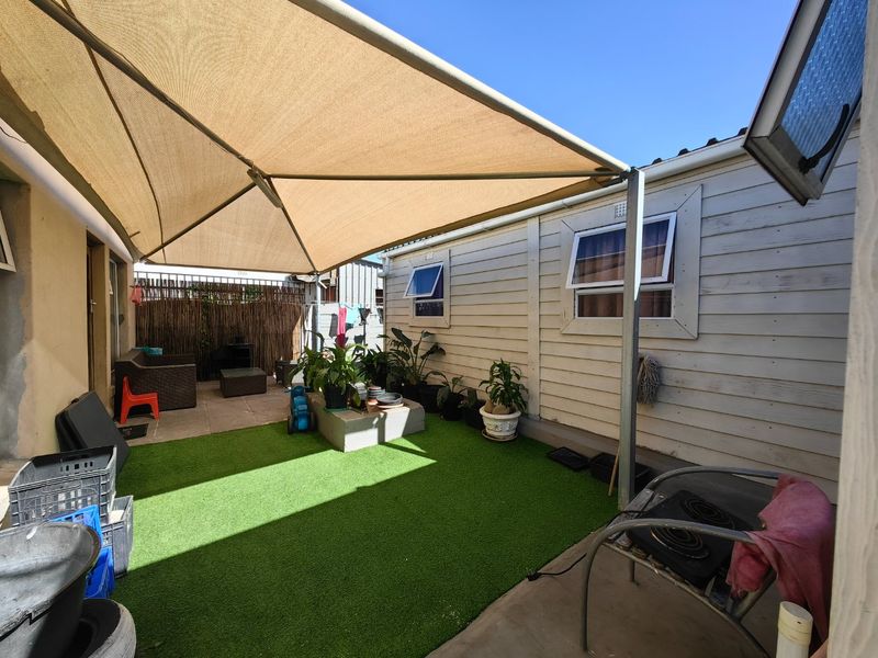 A covered outdoor patio area featuring a shade sail, artificial grass, and timber-clad exterior walls, providing a functional space for outdoor relaxation.