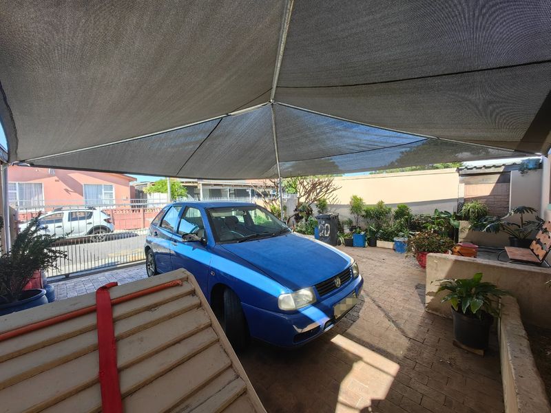 Outdoor paved parking area featuring a large overhead shade sail and secure boundary walling.