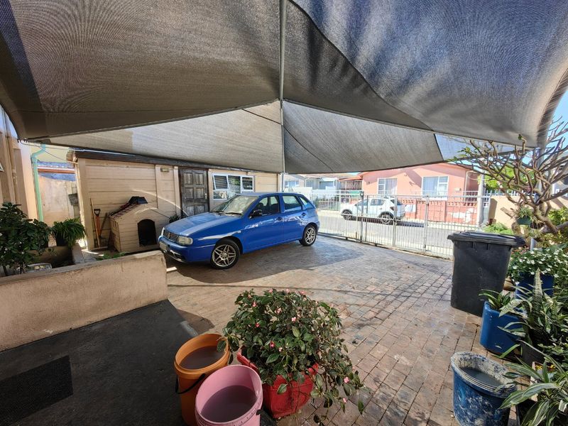 Outdoor paved parking area featuring a large overhead shade sail and secure metal gate access.