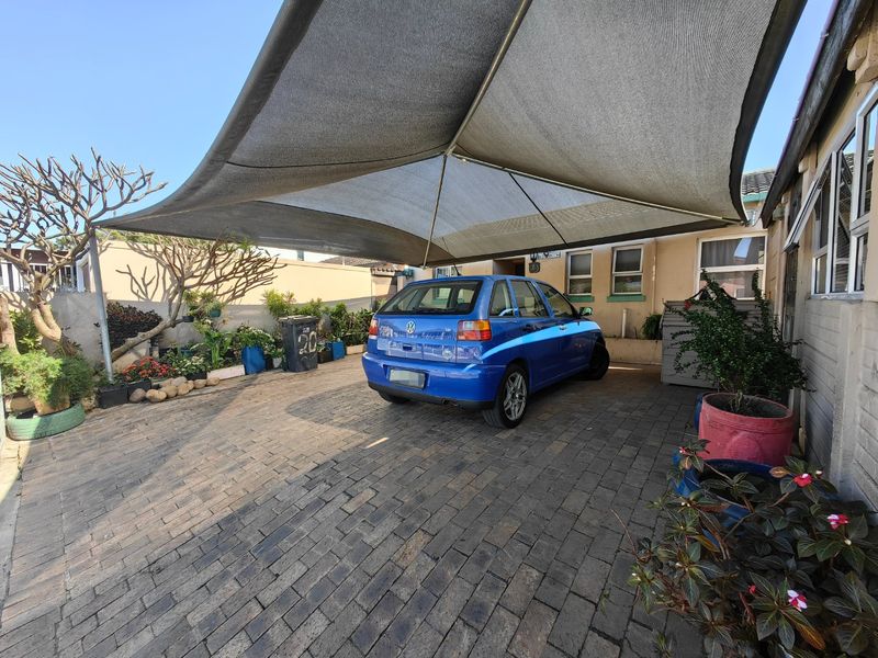 Front exterior area featuring a paved driveway and a large shade sail structure providing covered parking space.
