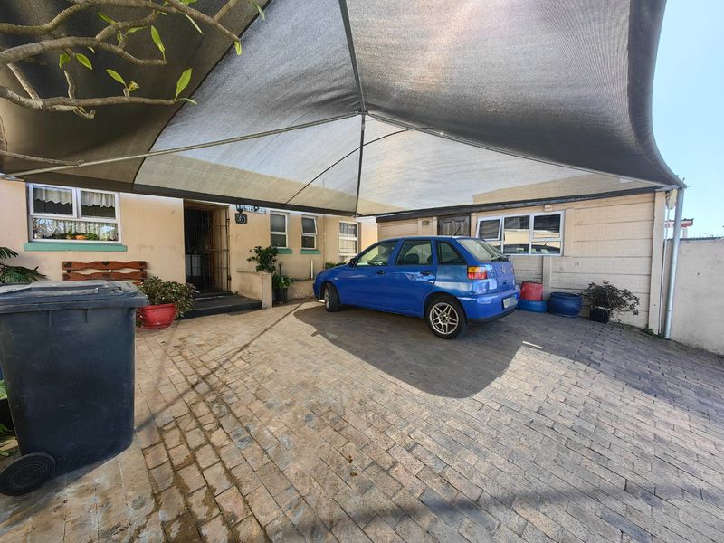 Front exterior view featuring a paved driveway, brick facade, and a large overhead shade sail providing covered parking.