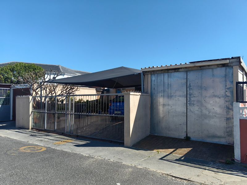 Front exterior view featuring a gated driveway, shade cloth carport, and a metal garage door with perimeter wall security.