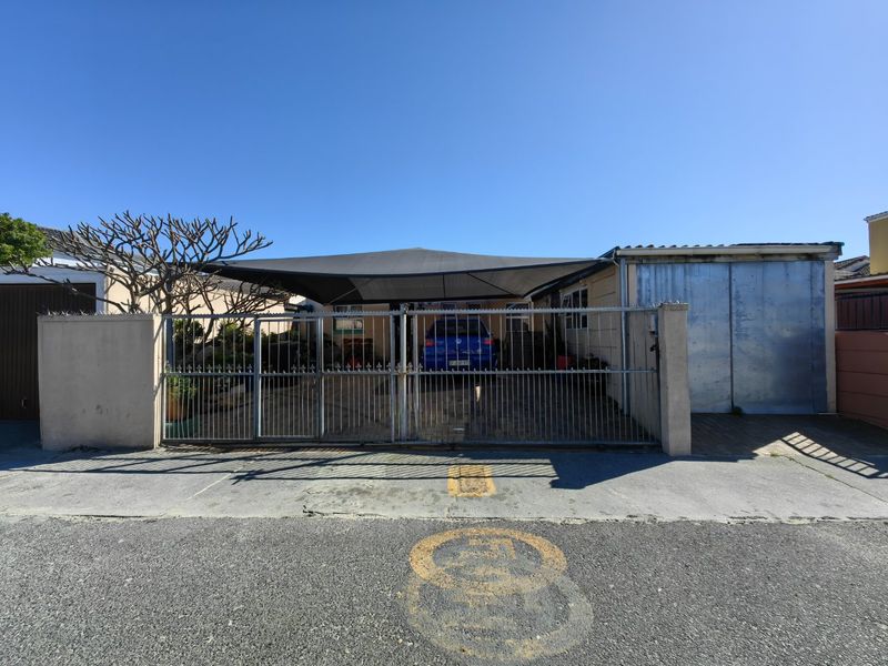 Front exterior view of the property featuring a metal security gate, concrete driveway, and a shade sail covering the parking area.