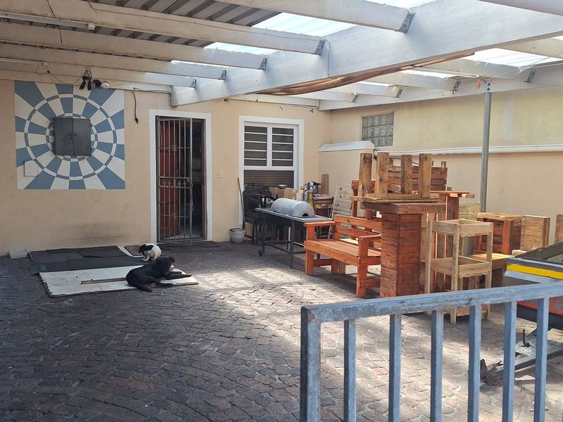 A covered outdoor patio area featuring paved flooring, exposed ceiling beams, and a security gate, offering potential for an improved entertainment space.