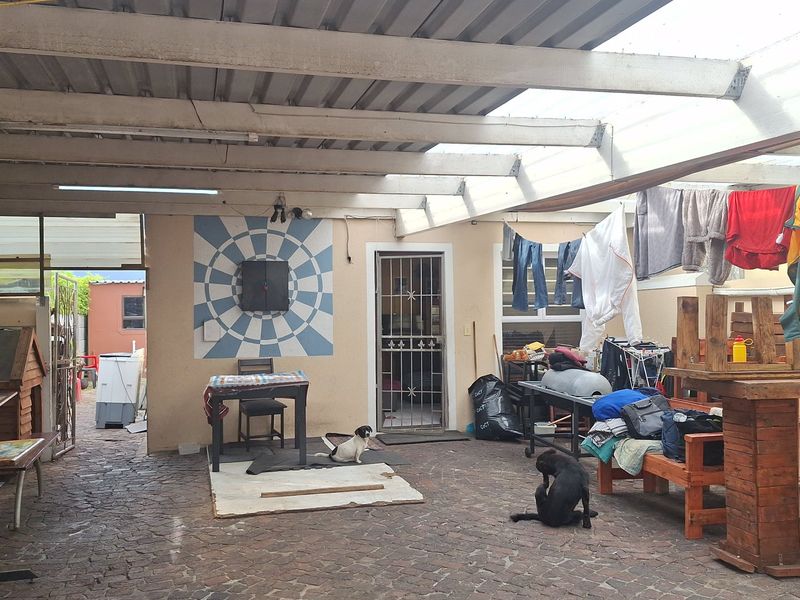 A covered outdoor patio area featuring paved flooring and a corrugated roof structure, providing a functional space for outdoor living.