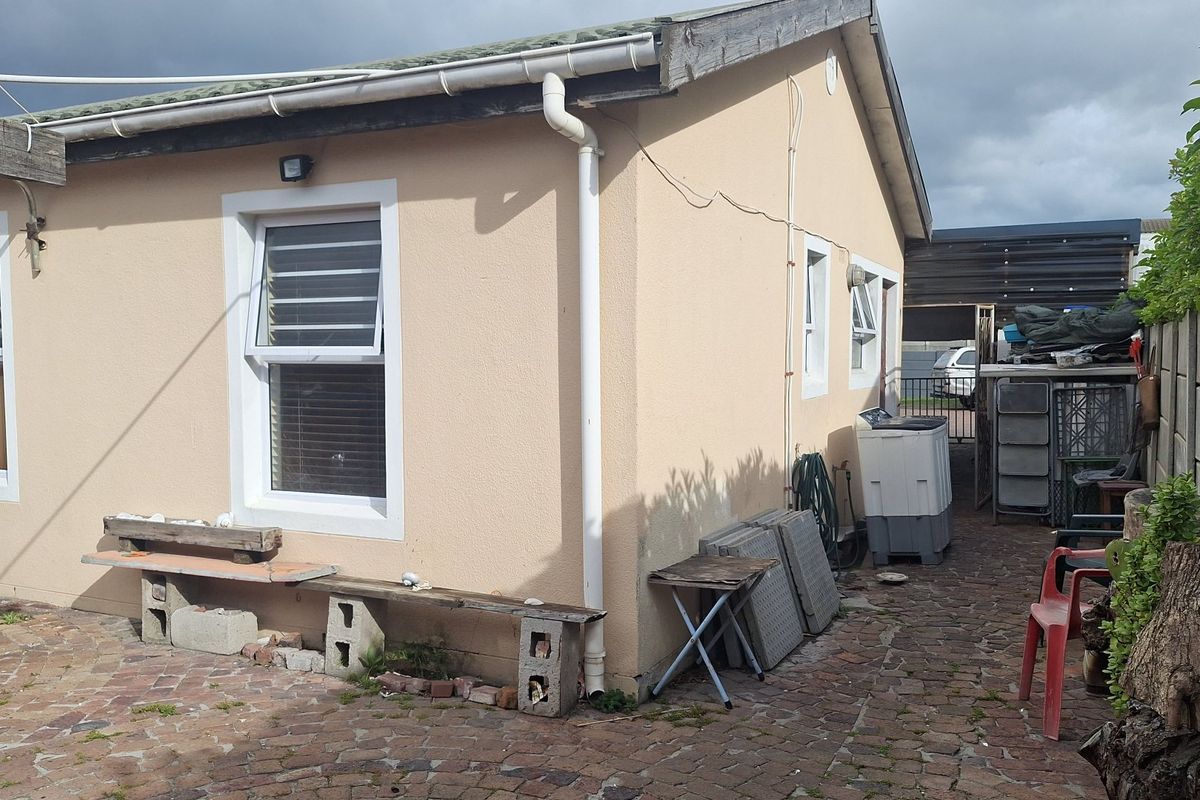 Rear exterior view of the property featuring a paved courtyard area, perimeter boundary wall, and functional guttering system.