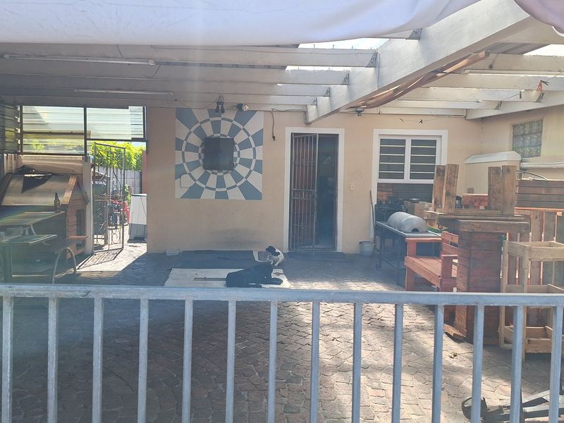 A covered outdoor patio area featuring a timber pergola structure, paved flooring, and a security gate entrance to the main house.
