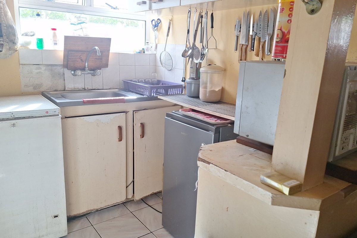 A compact kitchen area featuring a stainless steel sink, tiled backsplash, and original cabinetry in need of cosmetic updates.