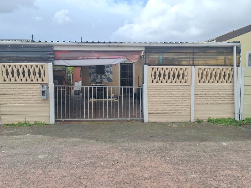 Front elevation of the property featuring a paved driveway, precast concrete boundary wall, and a metal security gate entrance.