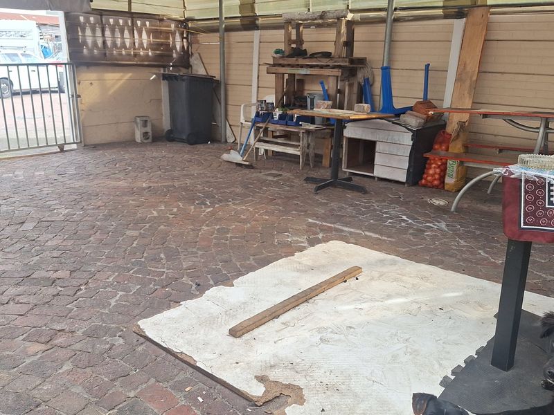 A covered outdoor patio area featuring brick paving and a metal roof structure, currently used as a utility and storage space.