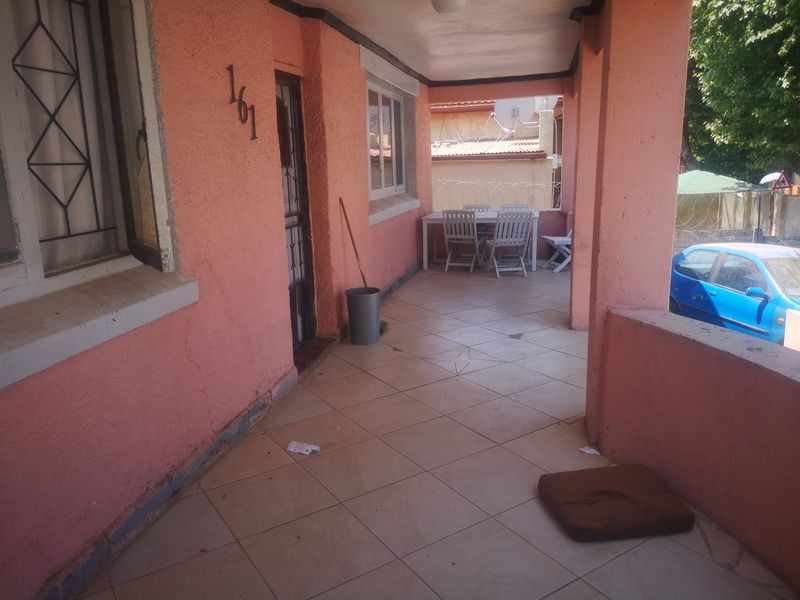 A covered front patio area featuring tiled flooring, security gate, and security bars on windows, requiring some maintenance and cosmetic updates.