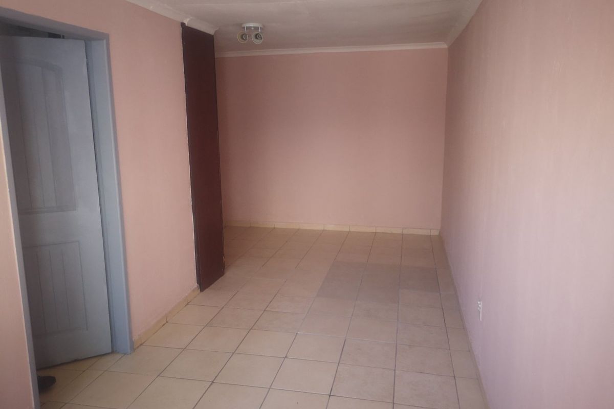 An empty, neutrally painted living area featuring tiled flooring and a ceiling-mounted spotlight fixture.